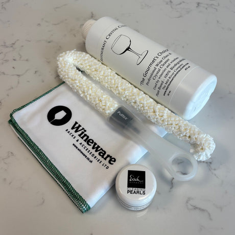 The Ultimate 4-Piece Wine Decanter Cleaning Set including a bottle of crystal cleaner, a flexible white decanter brush, a small container of cleaning pearls, and a branded cleaning cloth.