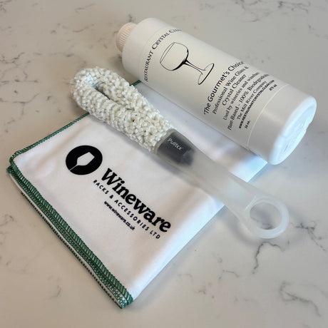 The Ultimate 3-Piece Wine Glass Cleaning Set featuring a white cleaning cloth, a flexible glass cleaning brush, and a bottle of crystal cleaner.