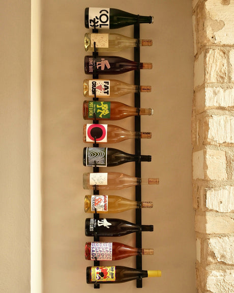 A VintageView Wall Mounted W Series 4 - 1220mm wine rack by VintageView displays up to thirty-six wine bottles horizontally, showcasing their colorful and unique labels against a white brick wall.