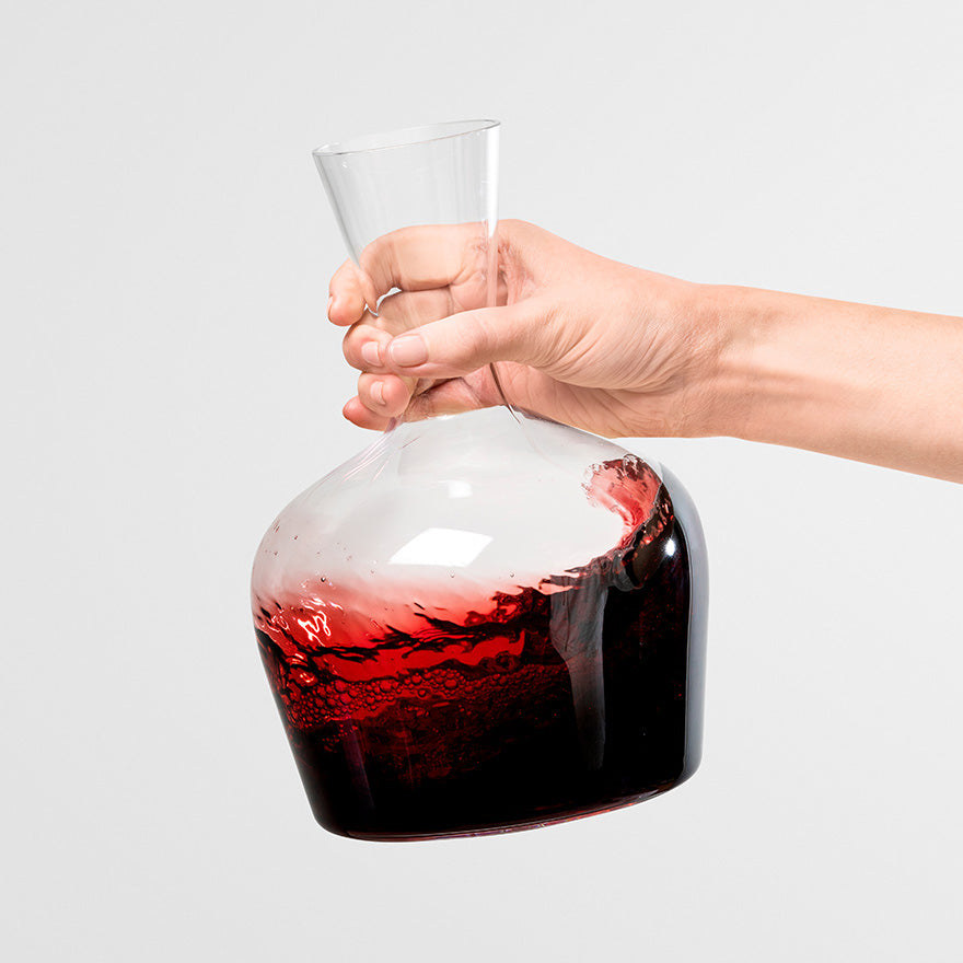 A hand swirls red wine in the Jancis Robinson x Richard Brendon Young Wine Decanter 1000ml against a plain white background, enhancing aeration.