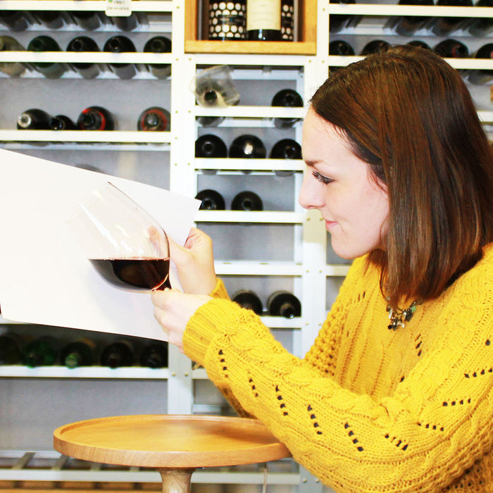 Woman in a yellow sweater examining the colour of the wine in a glass.