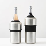 Two Huski Wine & Champagne Bottle Coolers by Huski, crafted in brushed stainless steel with black grips, each securely holding a wine bottle topped with a silver cap, are displayed on a white surface against a plain light background—an elegant solution for keeping your wine or champagne perfectly chilled for any occasion.