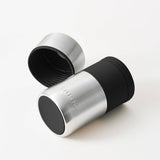 The Huski Wine & Champagne Bottle Cooler - Brushed Stainless Steel by Huski is displayed on a white background with its lid off and placed beside it. Featuring a black silicone grip, this insulated stainless steel cooler is perfect for keeping your wine or champagne at the ideal temperature.