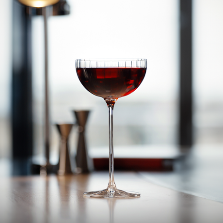 A Lehmann Glass La Creative Roma Cocktail Coupe 220ml filled with a red cocktail, set on a light-colored surface.